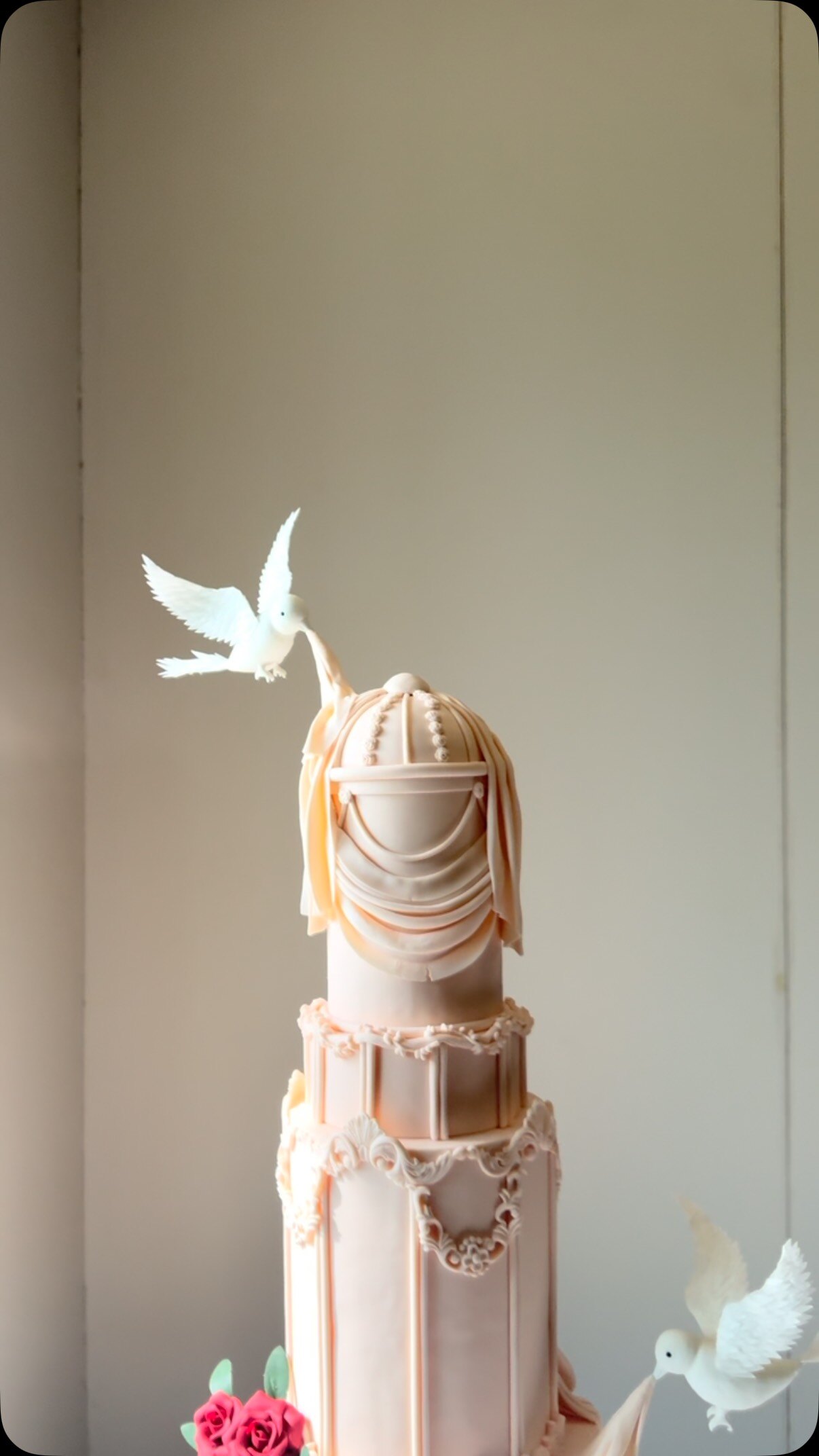 Tall blush wedding cake with white doves and draped pearls